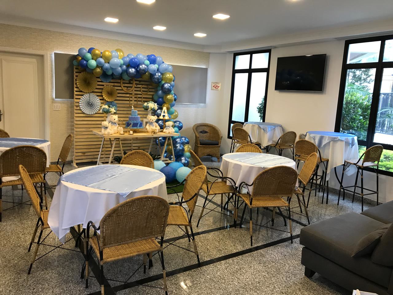 Decoração completa com painel de madeira, arco de bexigas azul, dourado e menta e mesas postas